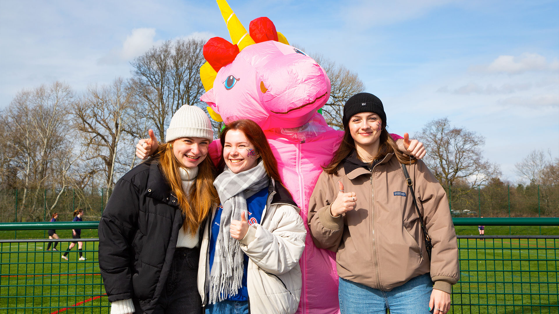 A photograph of three students posing with the unicorn mascot at Varsity 2023