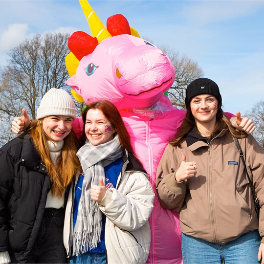 A photograph of three students posing with the unicorn mascot at Varsity 2023