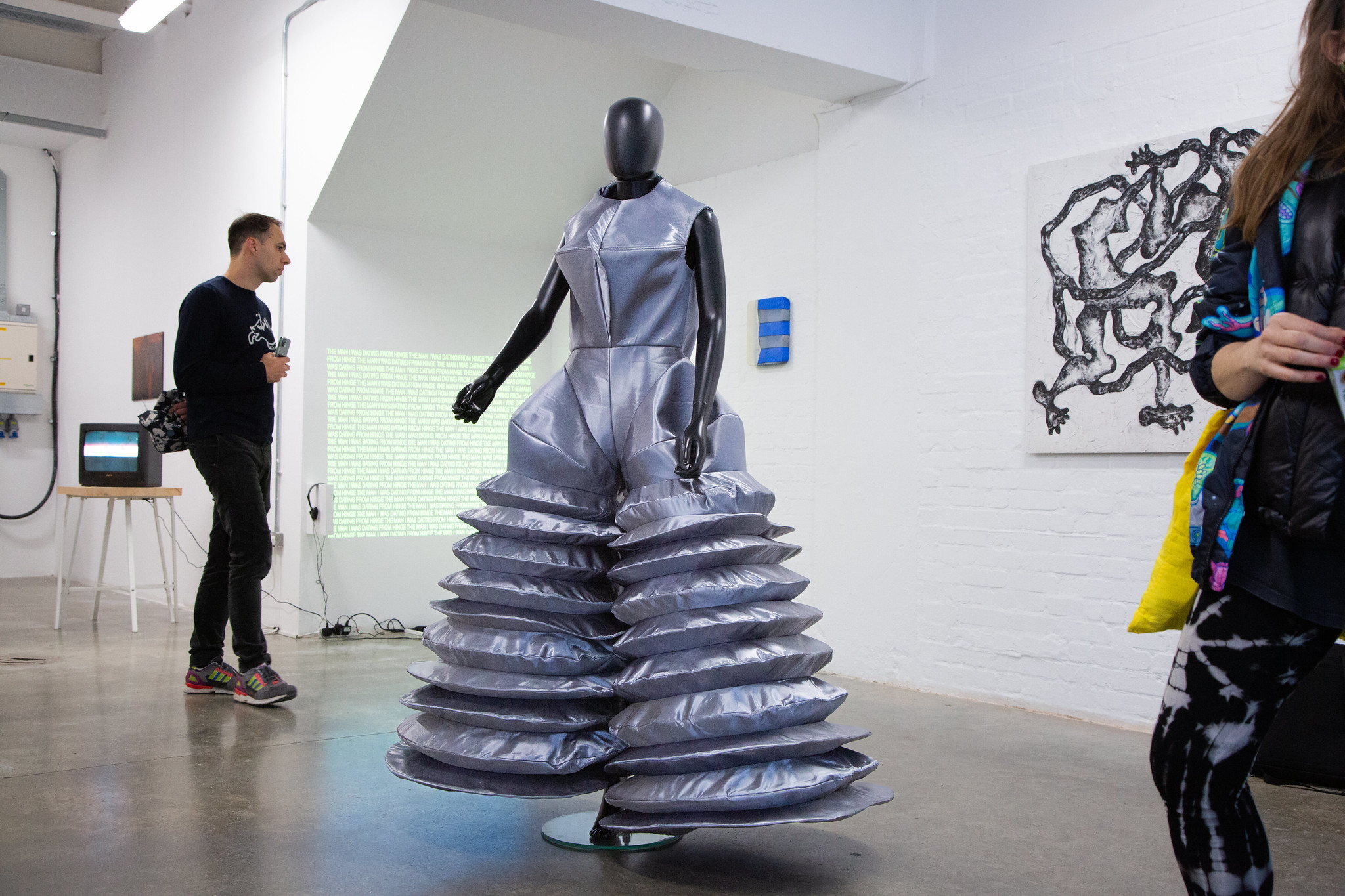 An image of a black mannequin in a silver jumpsuit with wide ringed legs.