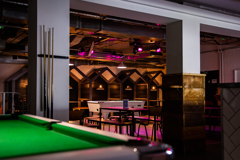 A wide angle of the pool table, raised seating and other tables