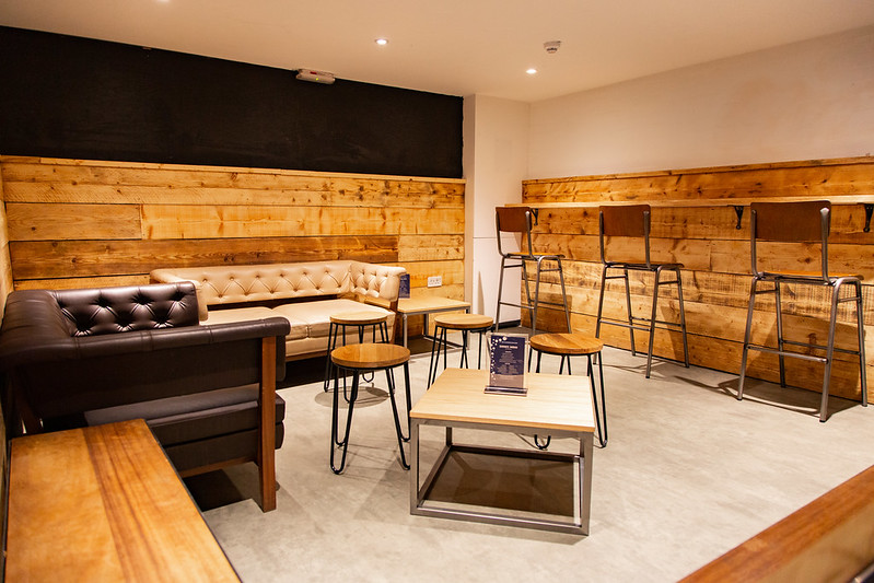 A seating area with bar stools, sofas and wooden panelling on the walls