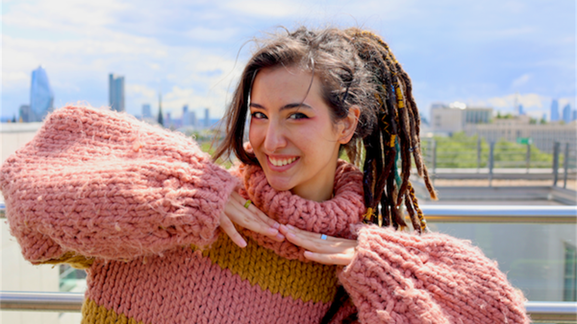 A person with long brown hair tied up in a ponytail, wearing a pink fluffy knitted jumper.