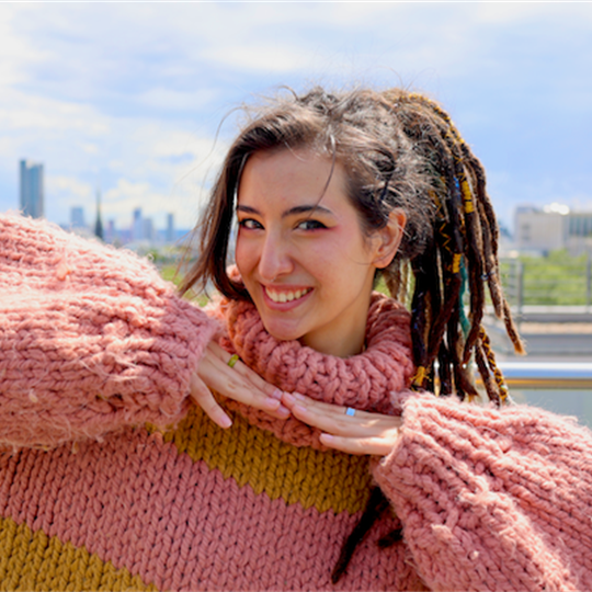 A person with long brown hair tied up in a ponytail, wearing a pink fluffy knitted jumper.